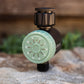 Watering timer with green dial sitting on a rock on a blurred natural background