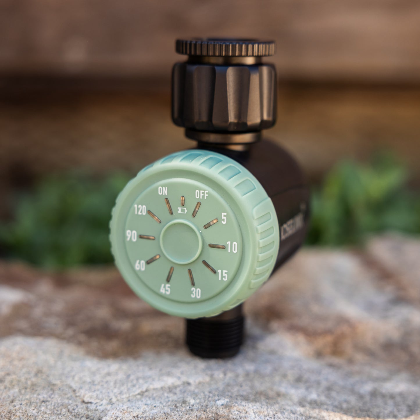 Watering timer with green dial sitting on a rock on a blurred natural background