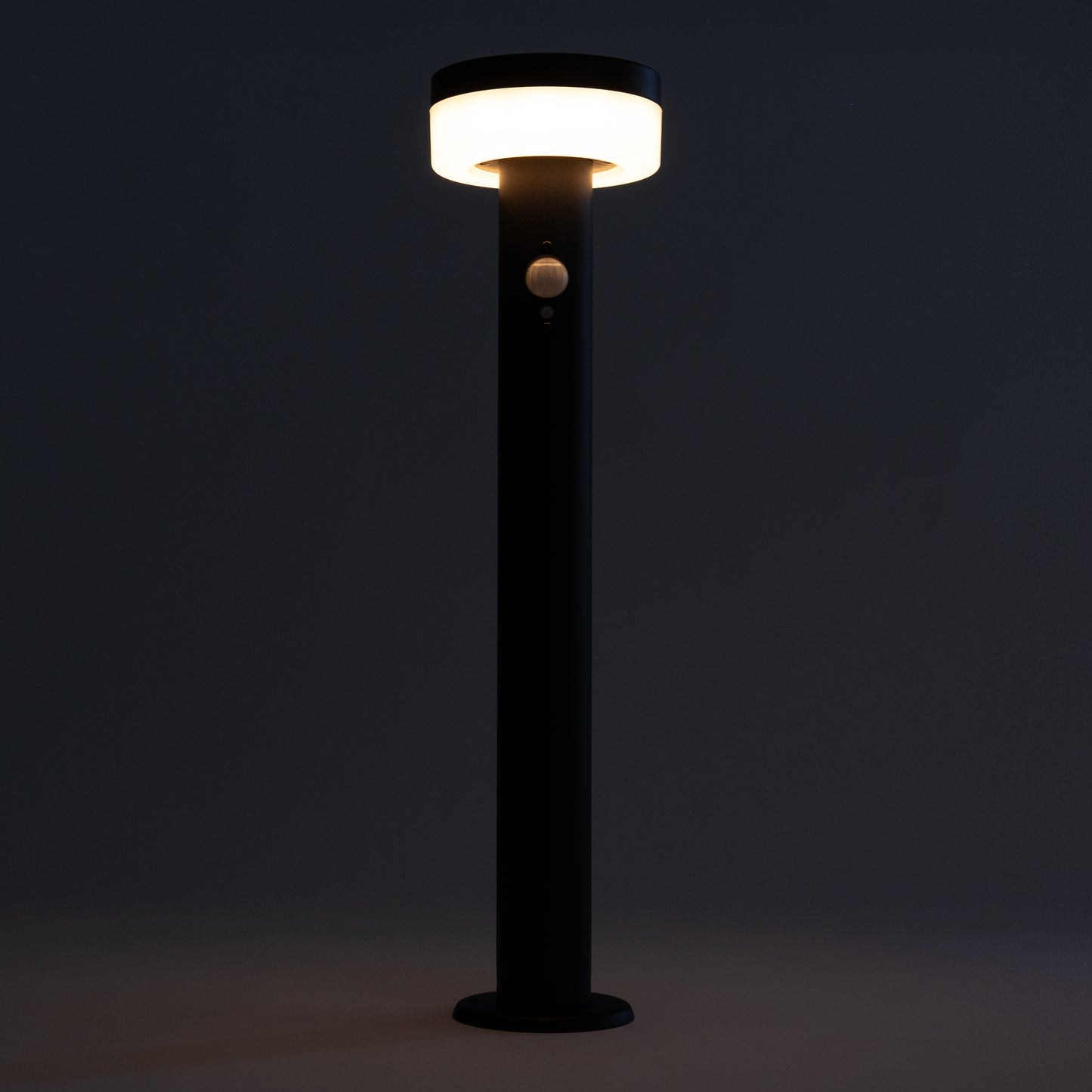 Black outdoor lamp post with illuminated light fixture against a dark background