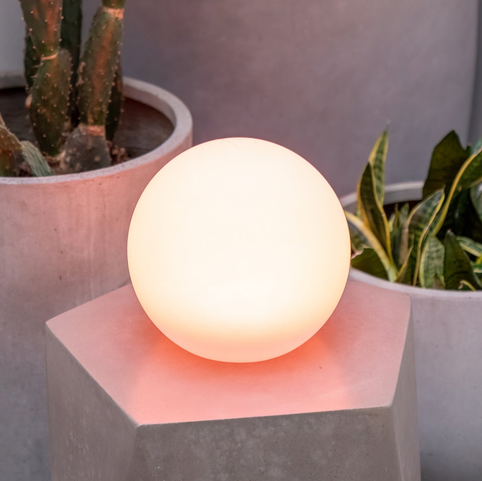 Solar Sphere 8in multicolor light on a concrete stand with potted plants in the background