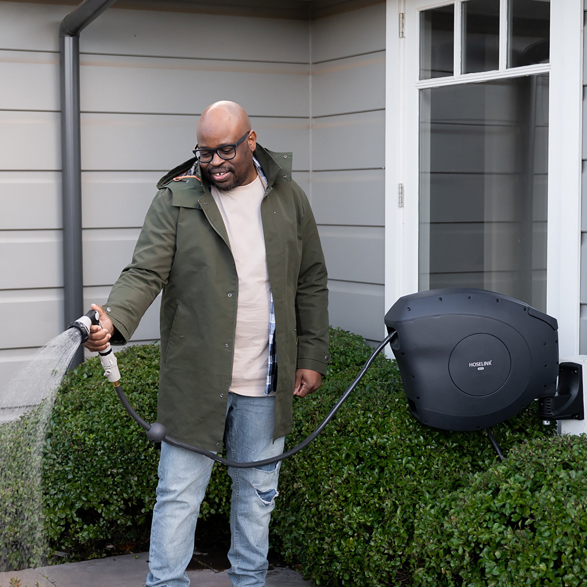 man watering his front yard with a charcoal retractable hose reel