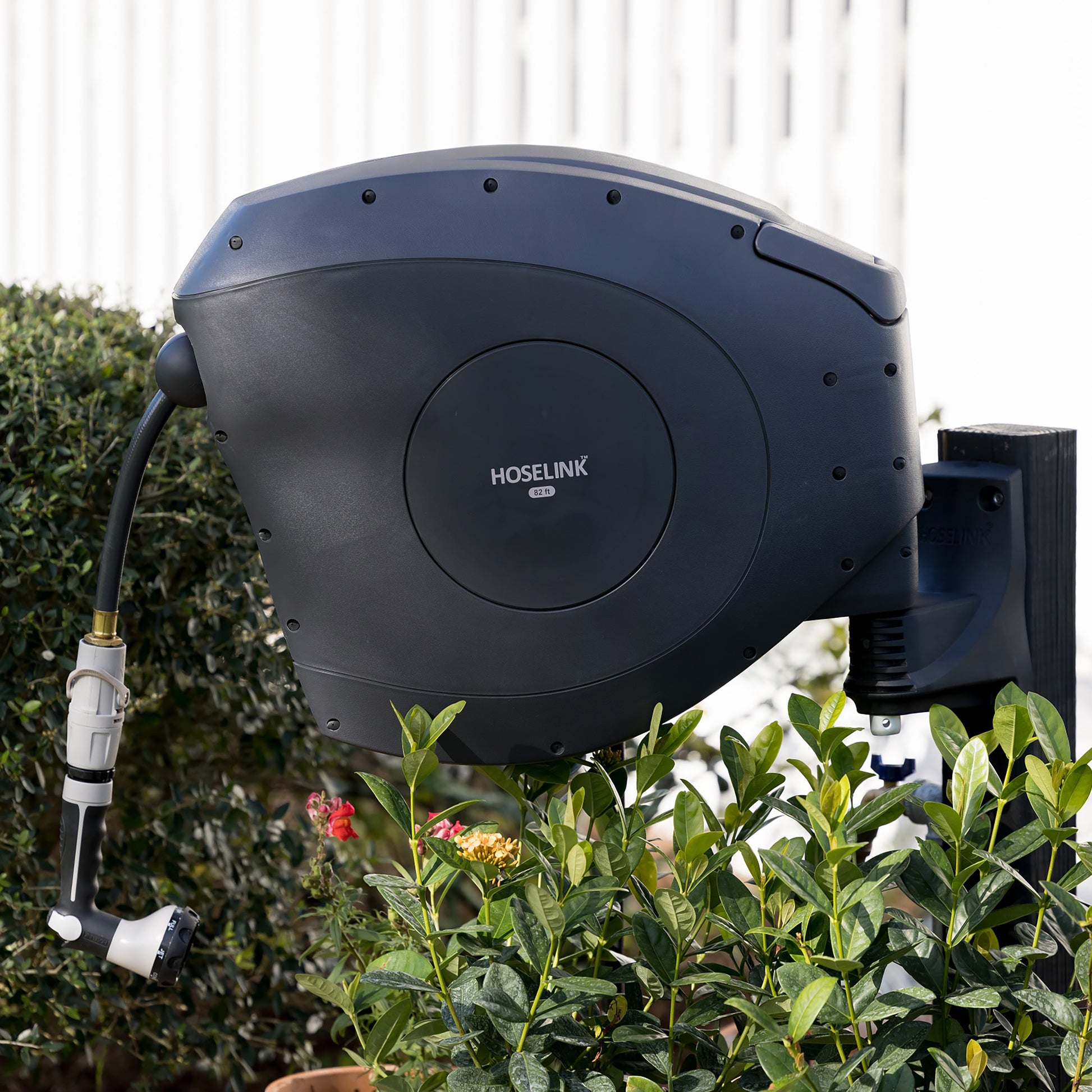 charcoal hose reel mounted on a post in a garden with a white fence in the background