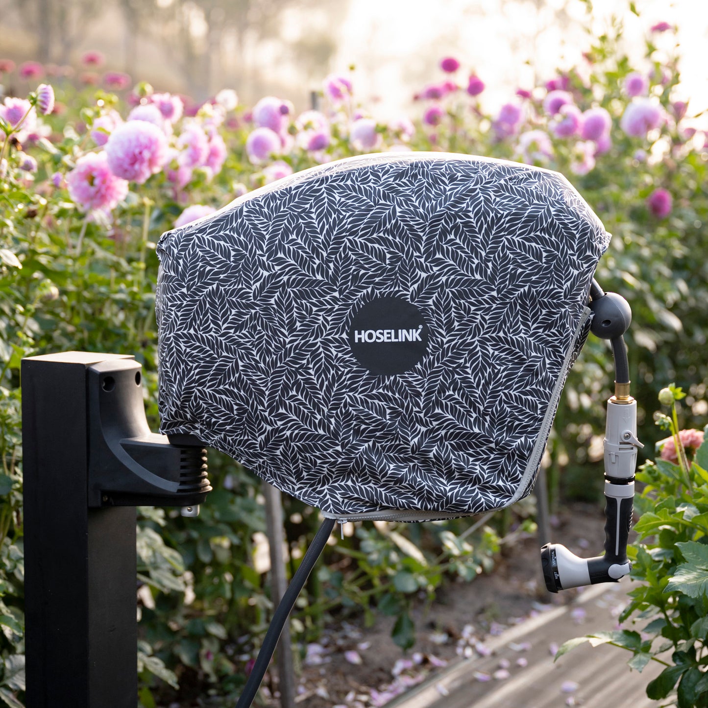 charcoal hose reel mounted on a post amongst a flower garden with a charcoal fern hose reel cover over it