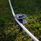 A beige hose travelling along a charcoal ground hose guide spiked into grass.