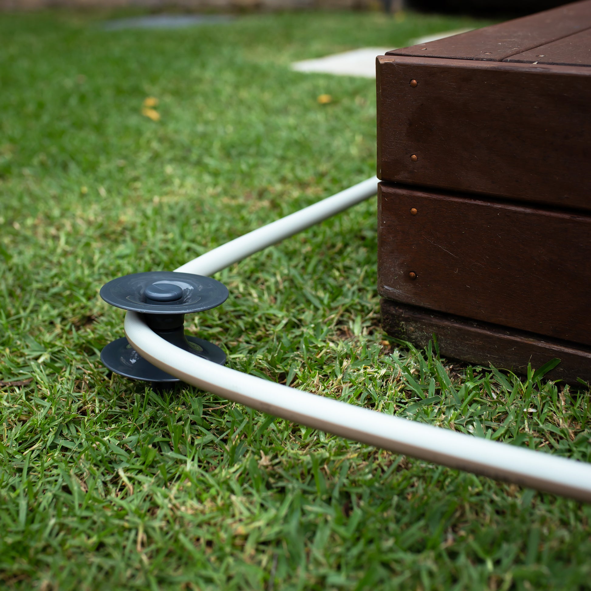 A beige hose around a ground hose guide in grass, away from the corner of a deck.