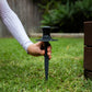 Close up of a person's hand about to spike a ground hose guide into the lawn.