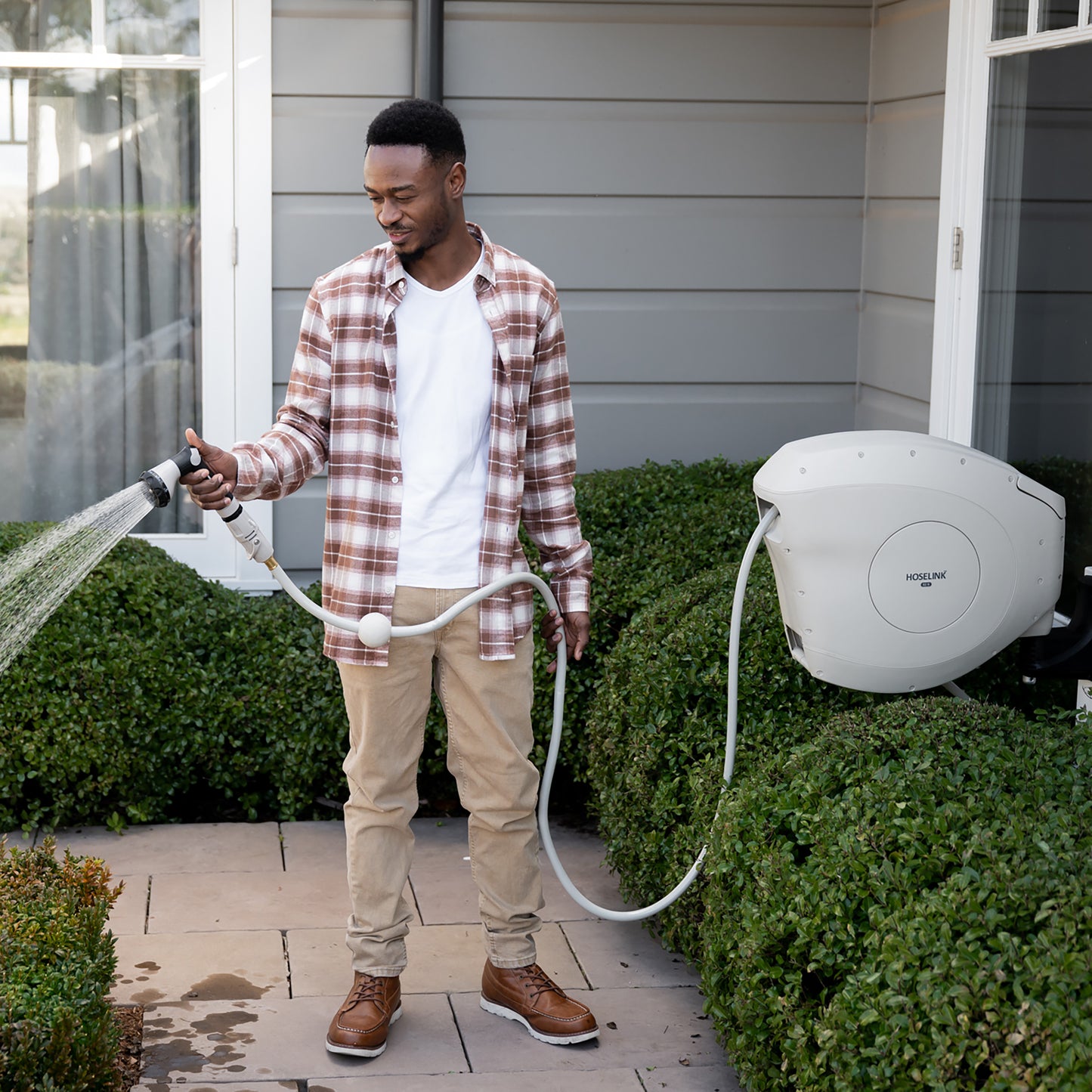 man standing on the pavement watering the garden in his front yard