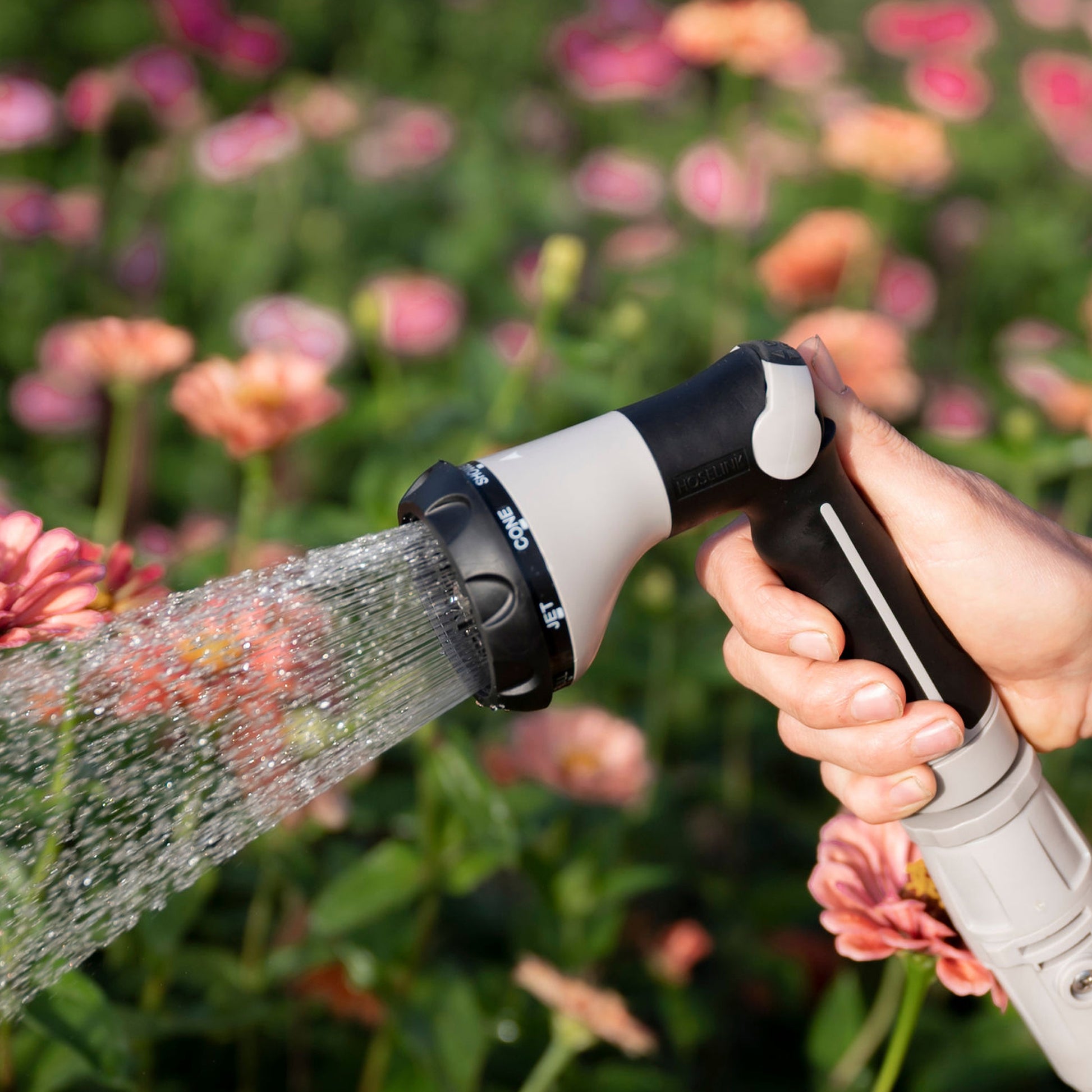 spray gun being held while watering the garden with pink flowers in the background