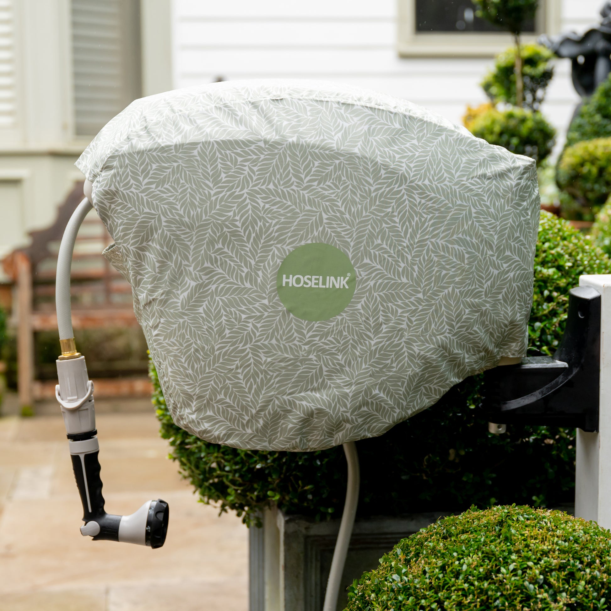 beige hose reel mounted between hedges with a green fern hose reel cover over it